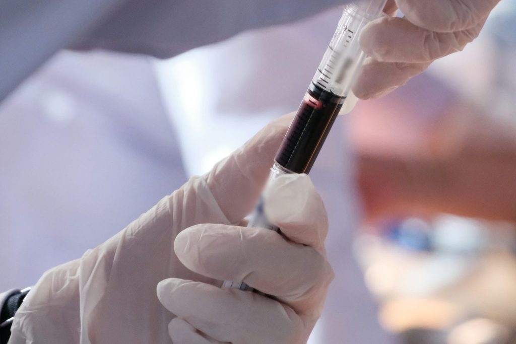 Gloved hands transferring a blood sample from a syringe into a collection tube for DUI blood alcohol testing