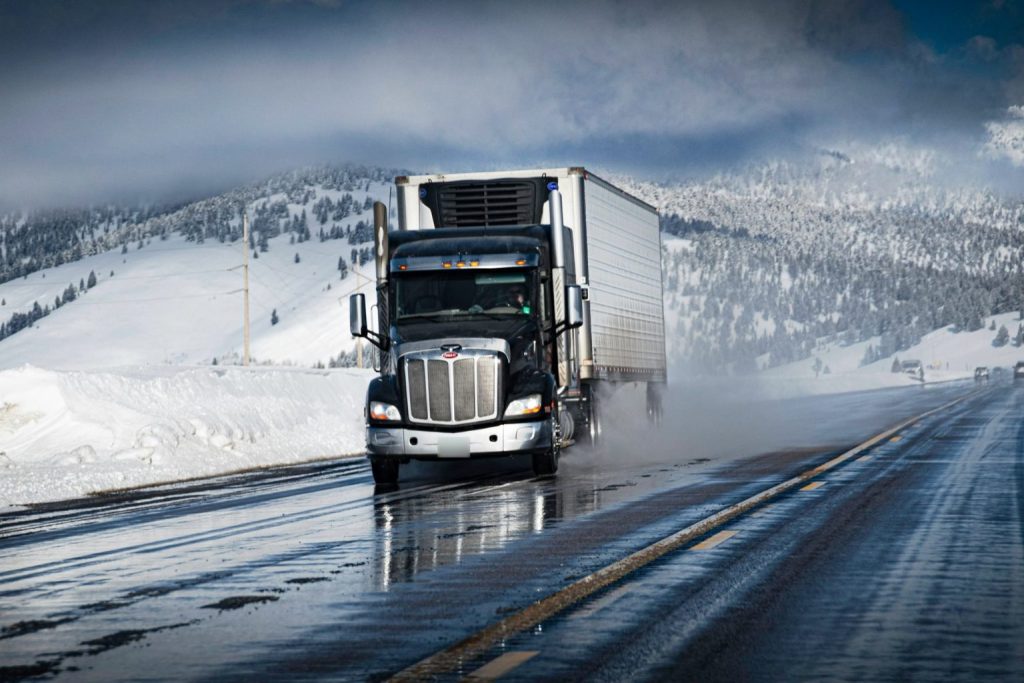 Tractor-trailer driving on a wet, snow-lined mountain highway in winter
