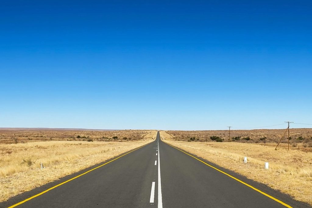 Straight highway running to the horizon across flat, open grassland under a blue sky